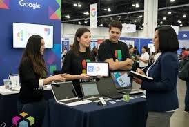 Demostración interactiva de herramientas de Google Workspace en el stand de G Nerd. El personal enseña soluciones en laptops y tabletas a una visitante.
